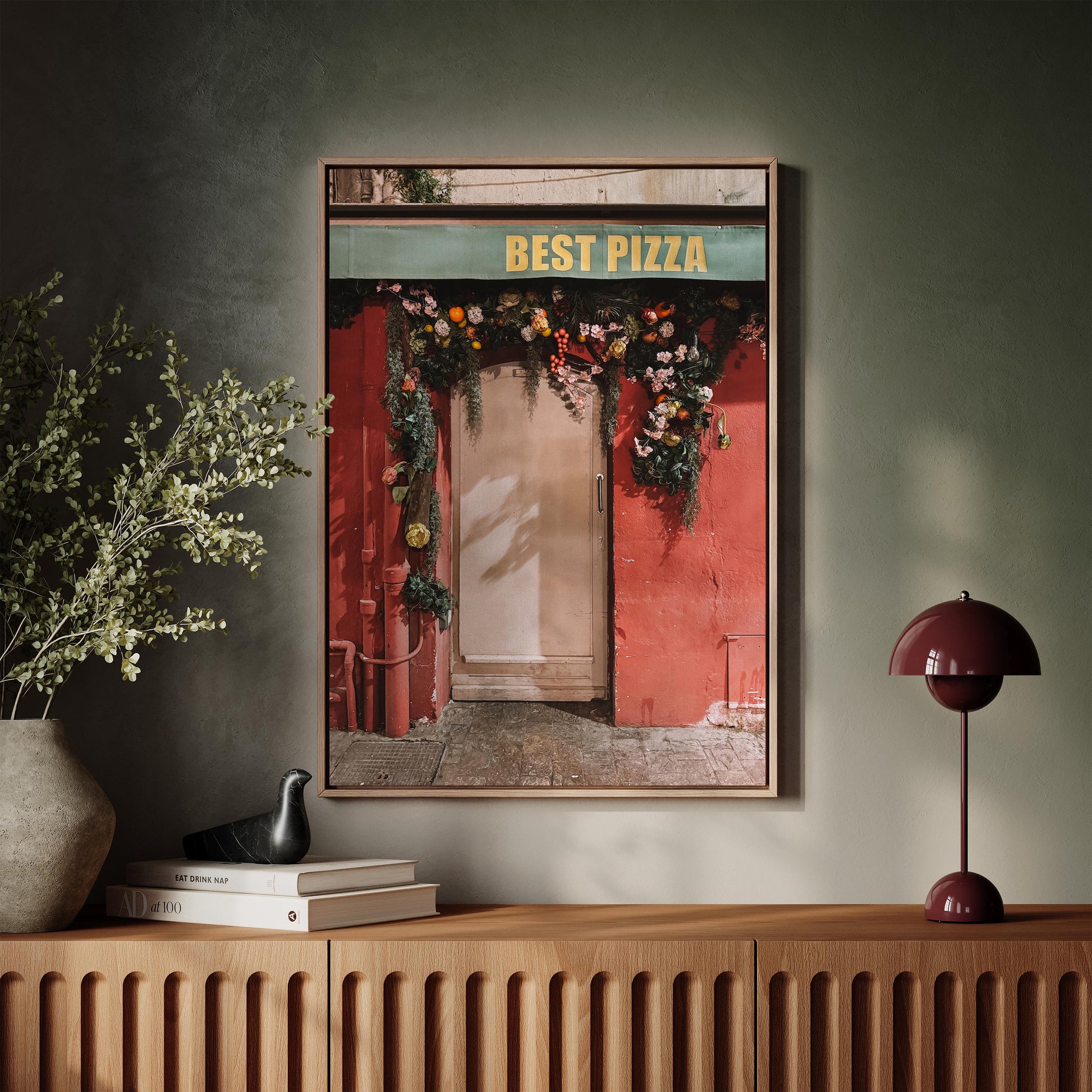 Framed artwork of a pizza shop entrance on a wall above a wooden console table.