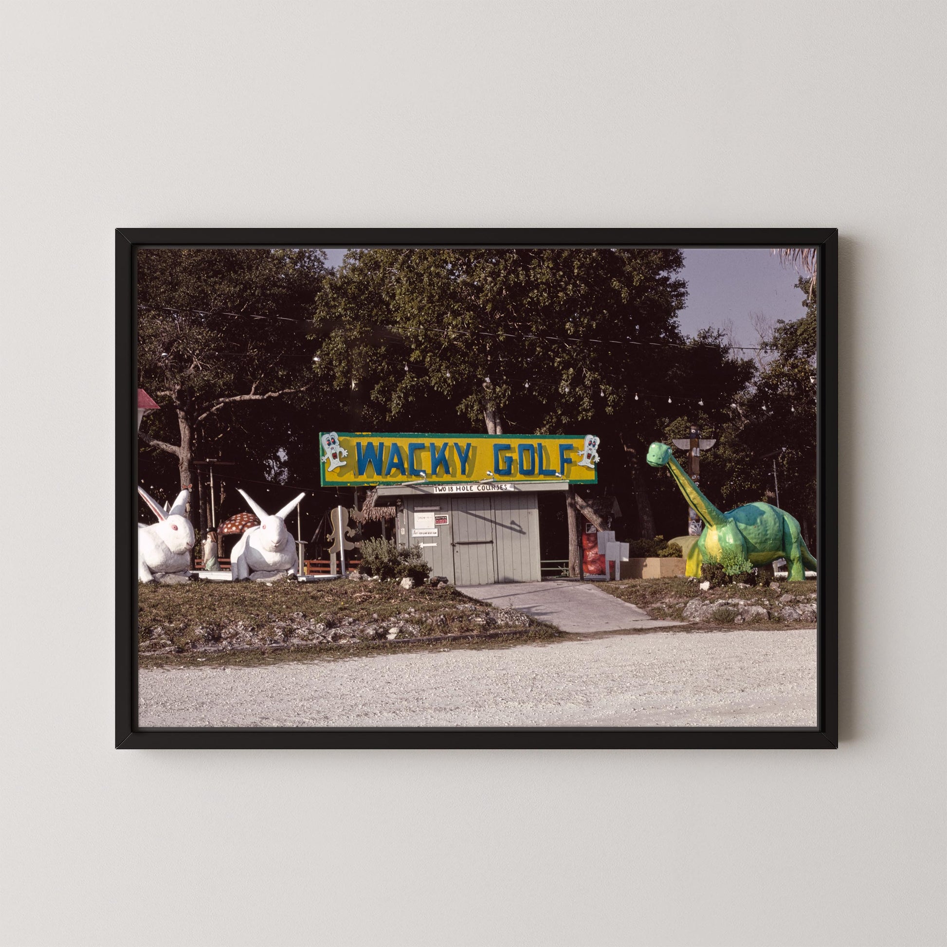 Framed photograph of a golf course with a 'Wacky Golf' sign and cartoonish dinosaur and rabbit statues.