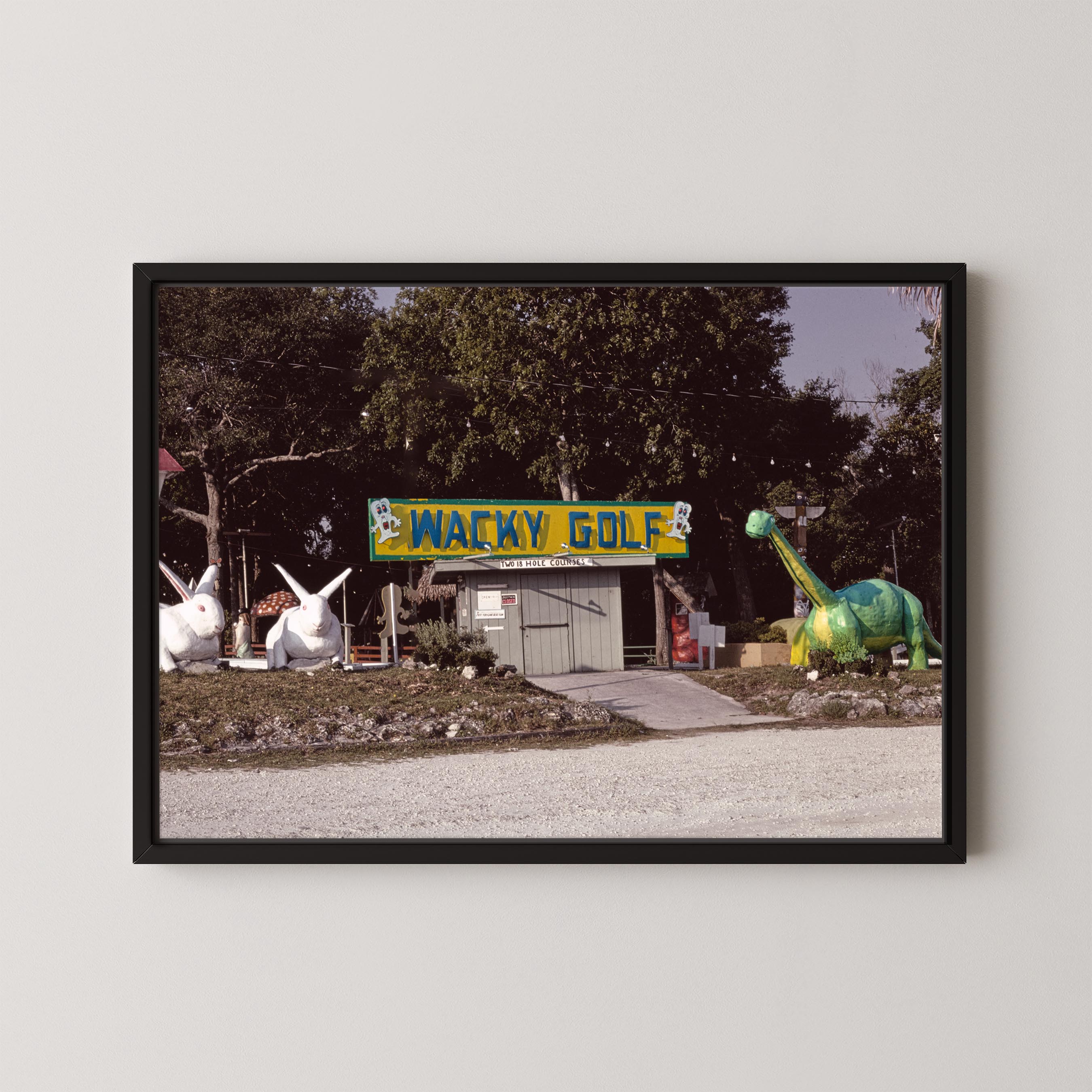 Framed photograph of a golf course with a 'Wacky Golf' sign and cartoonish dinosaur and rabbit statues.