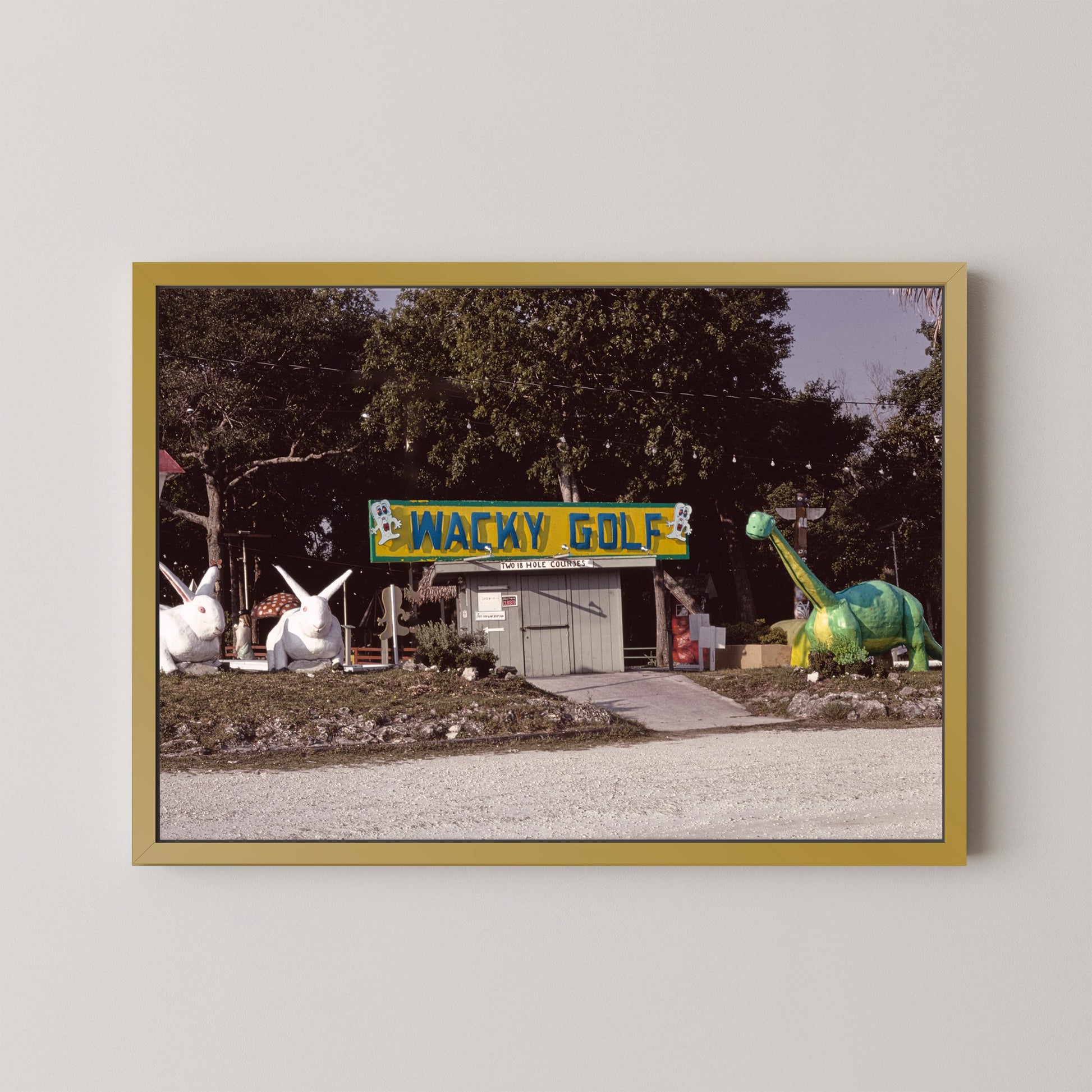 Framed photograph of a golf course with a 'Wacky Golf' sign and cartoonish dinosaur and rabbit statues.