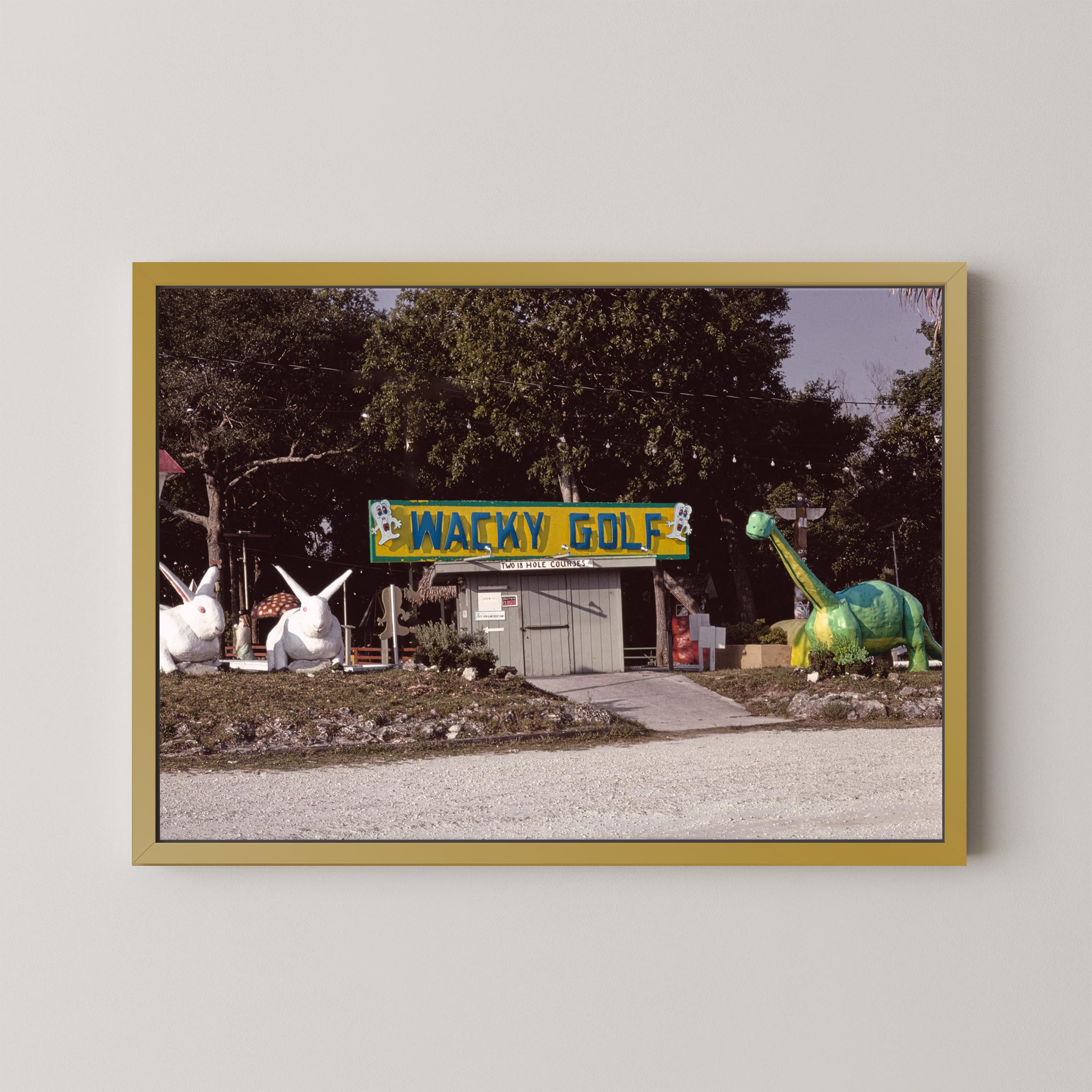 Framed photograph of a golf course with a 'Wacky Golf' sign and cartoonish dinosaur and rabbit statues.
