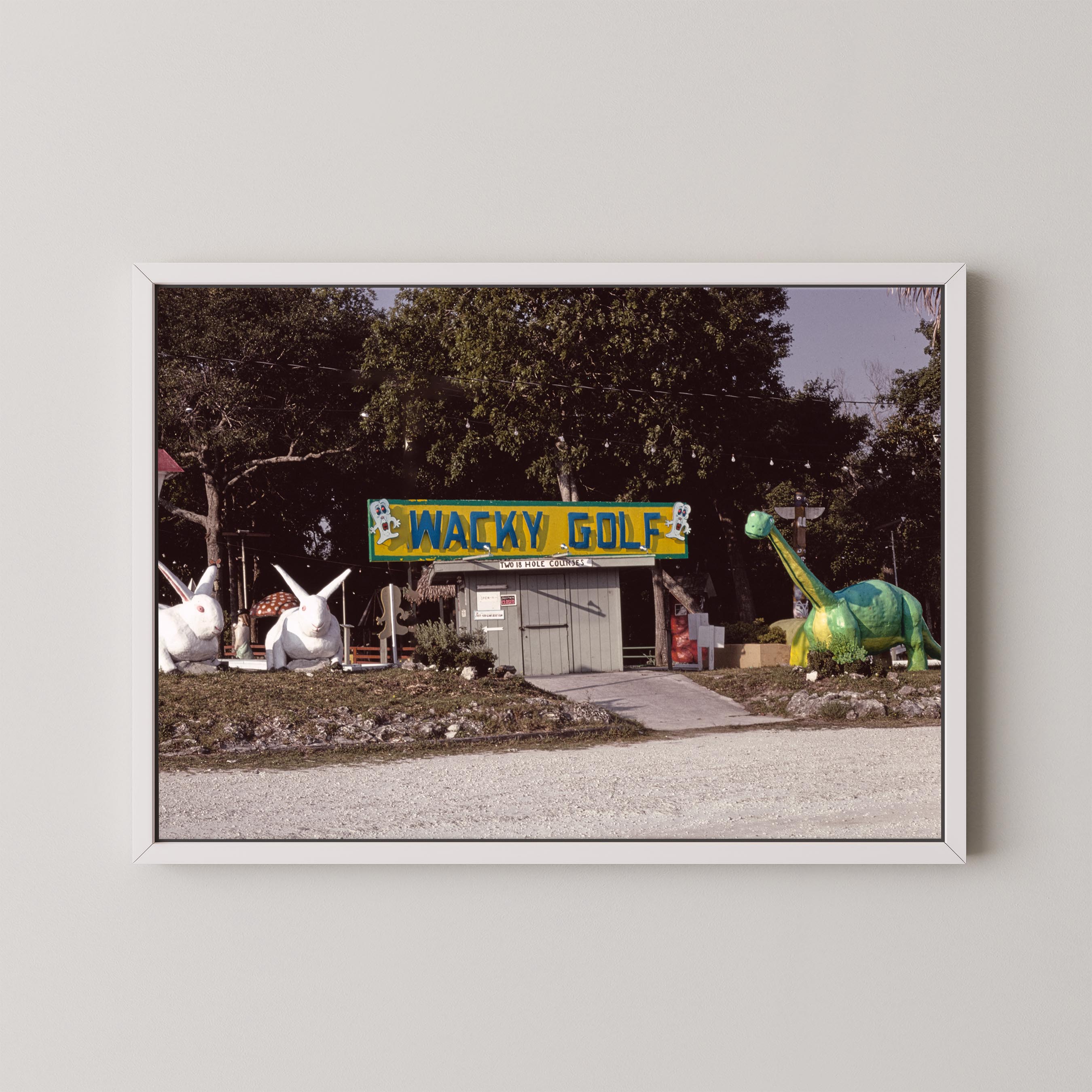 Framed photograph of a golf course with a 'Wacky Golf' sign and cartoonish dinosaur and rabbit statues.