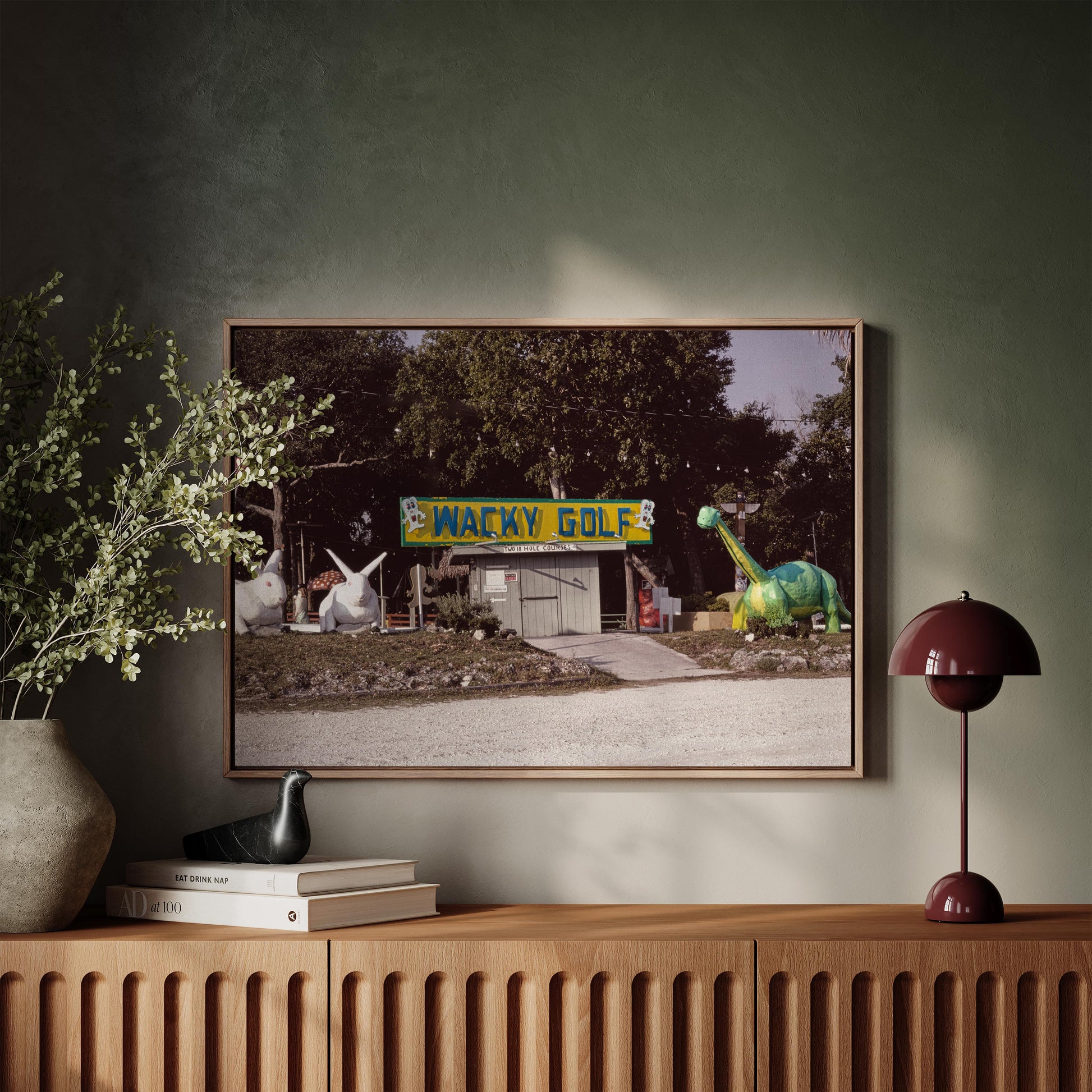 Framed artwork of a golf course with cartoon characters on a wall above a wooden console table.