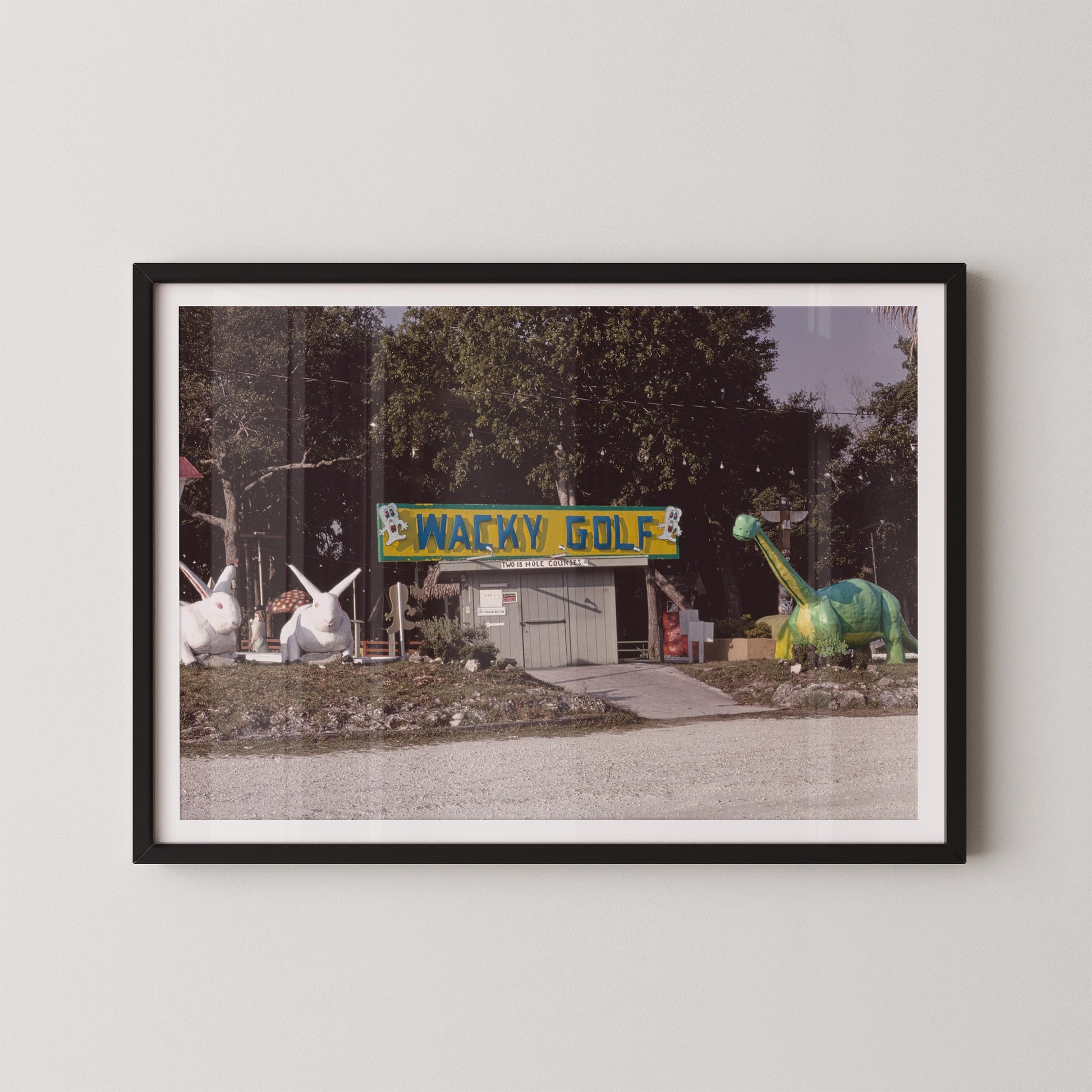 Framed photograph of a Wacky Golf sign with cartoonish sculptures on a white wall.