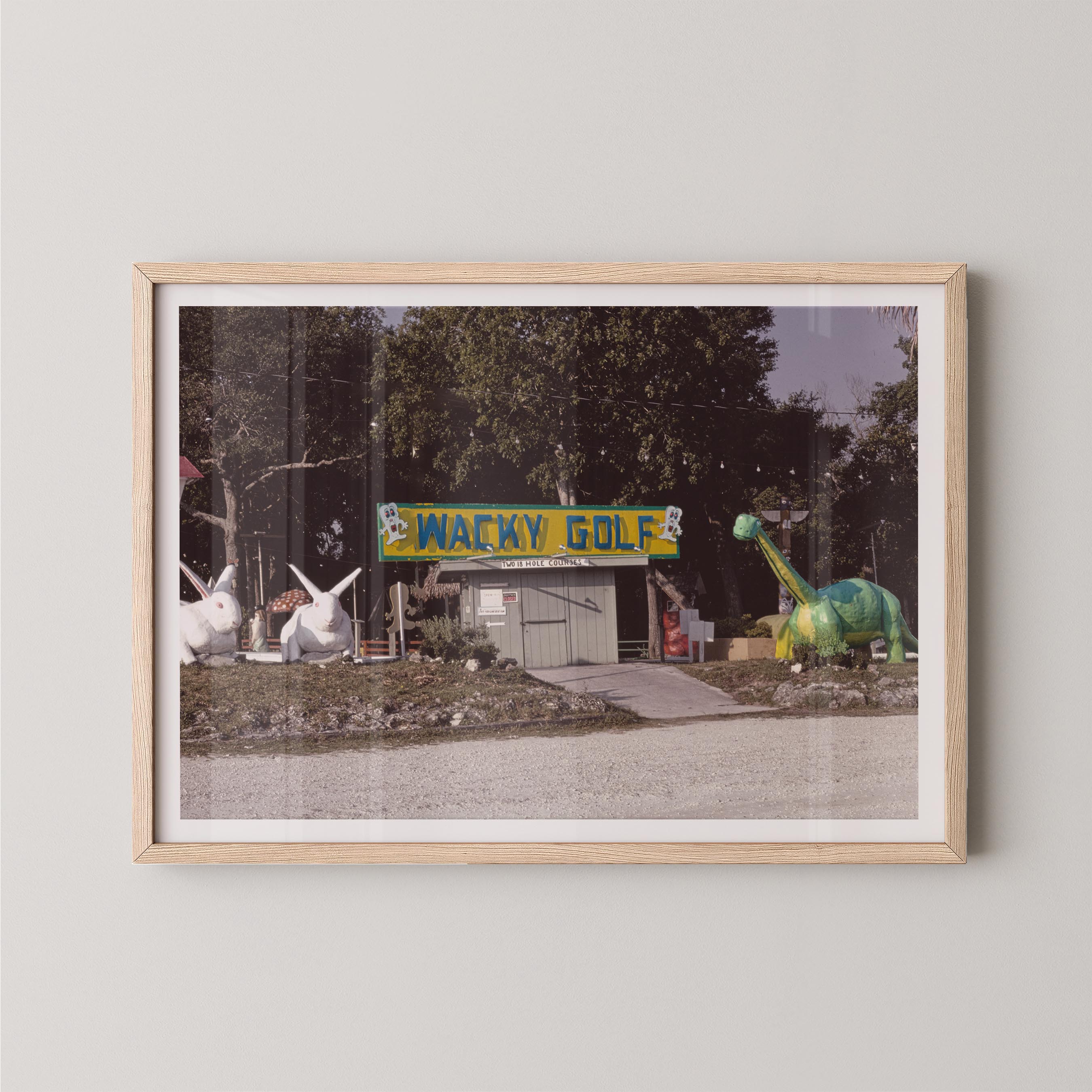 Framed photograph of a Wacky Golf sign with cartoonish sculptures on a gray wall.